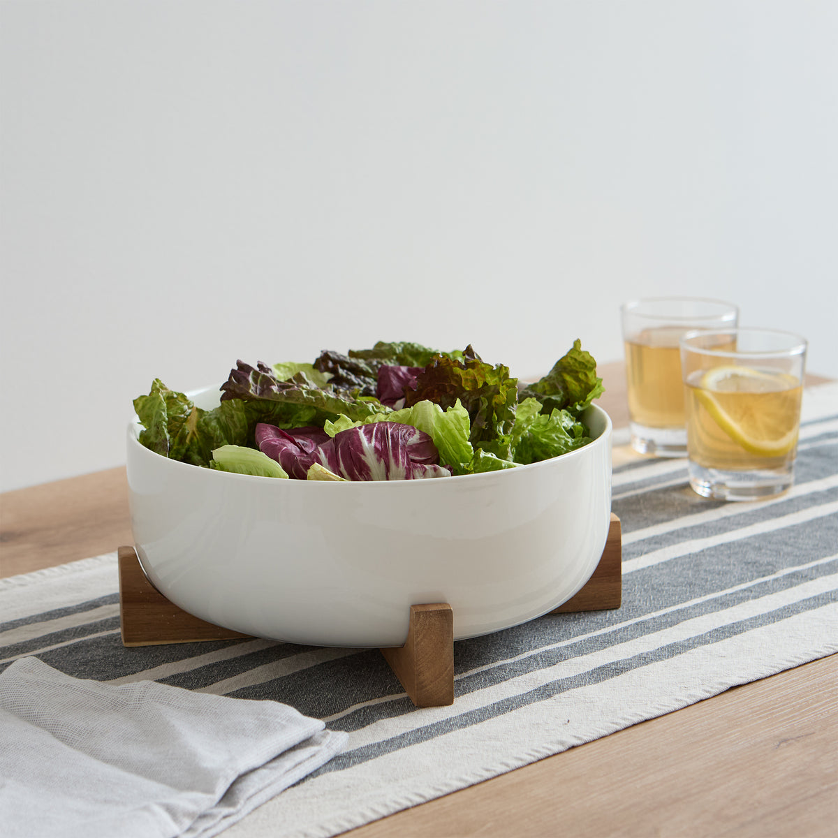 Serving bowl on acacia stand with salad on a table runner